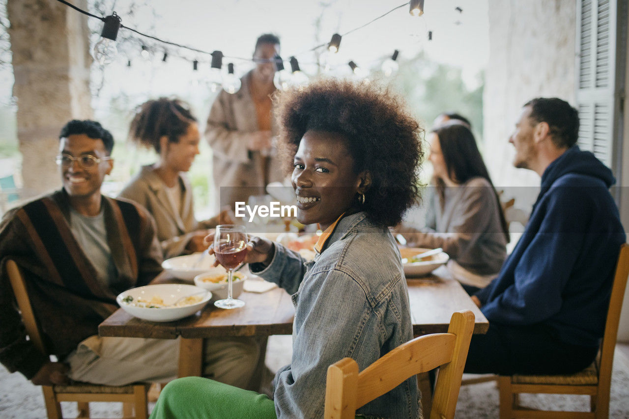 Portrait of happy woman with afro hairstyle holding wineglass during dinner party in patio