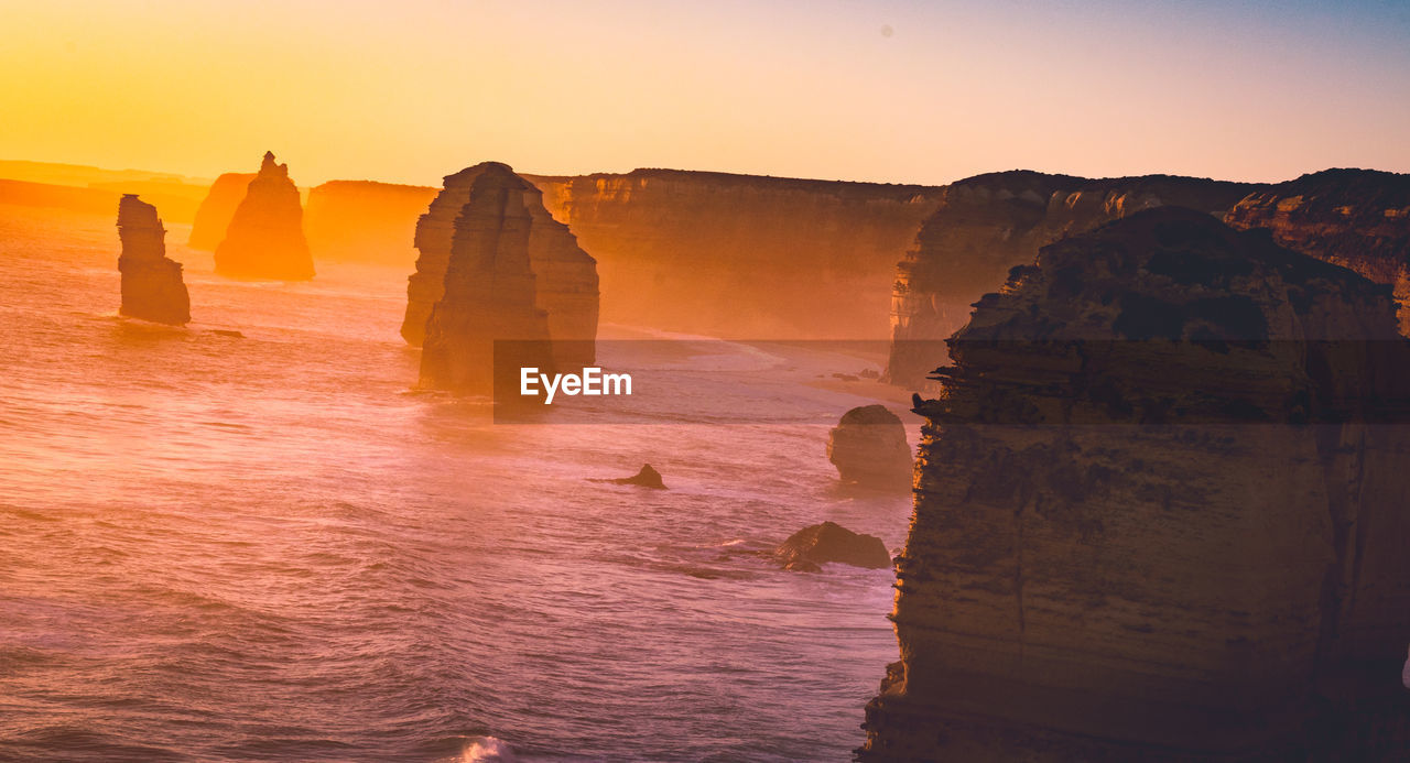 ROCK FORMATIONS ON SEA AGAINST SKY DURING SUNSET