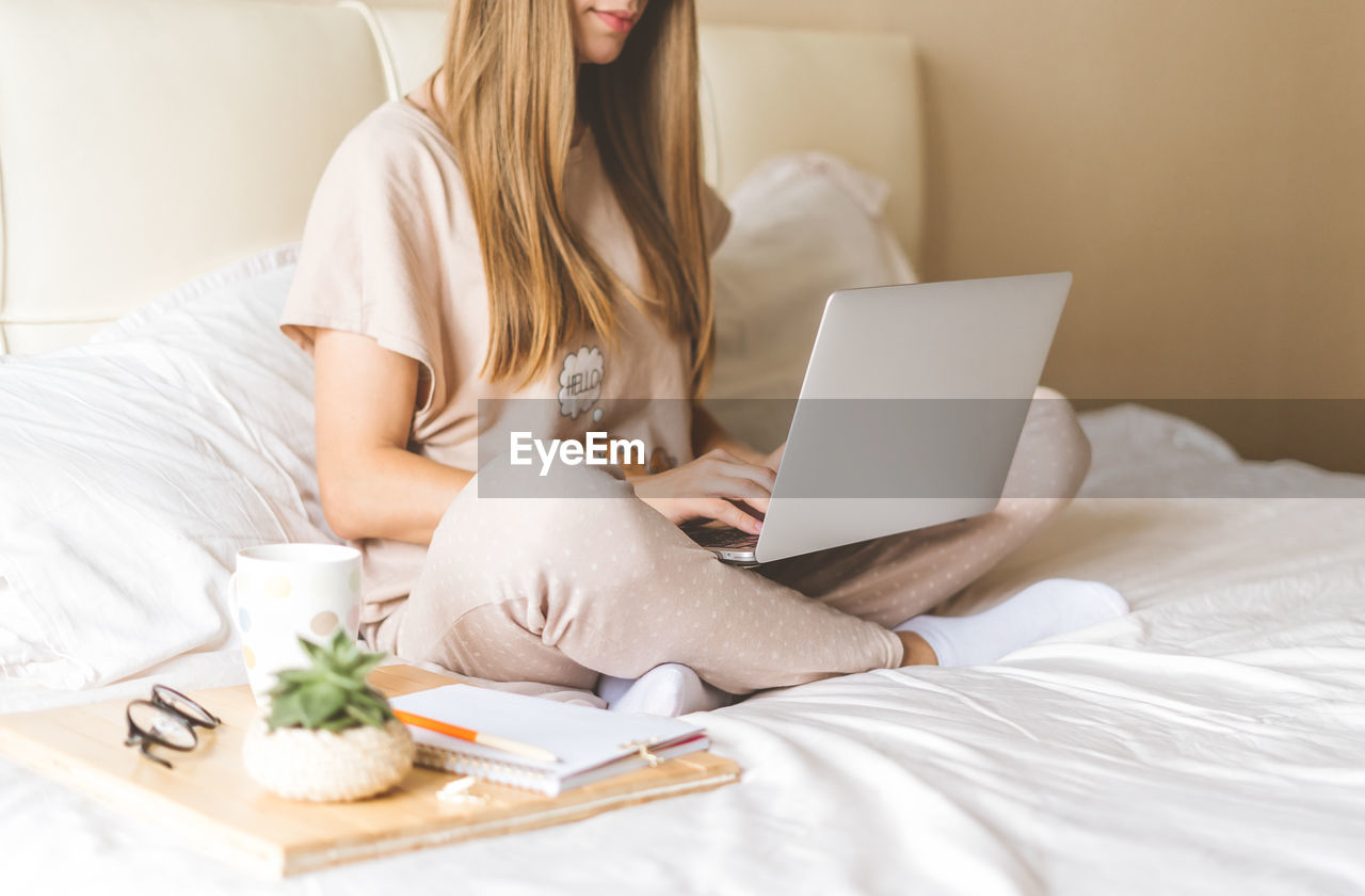 Low section of woman using laptop while sitting on bed at home