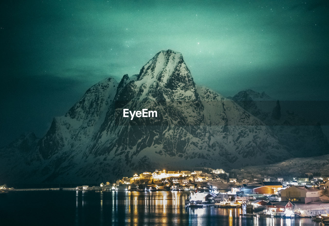 Scenic view of sea by snowcapped mountains against sky at night