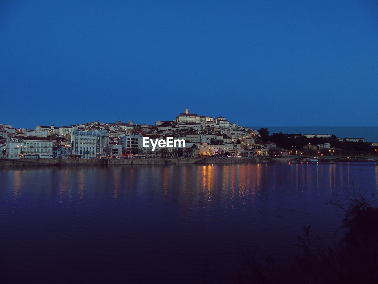 Illuminated cityscape by sea against clear blue sky at night