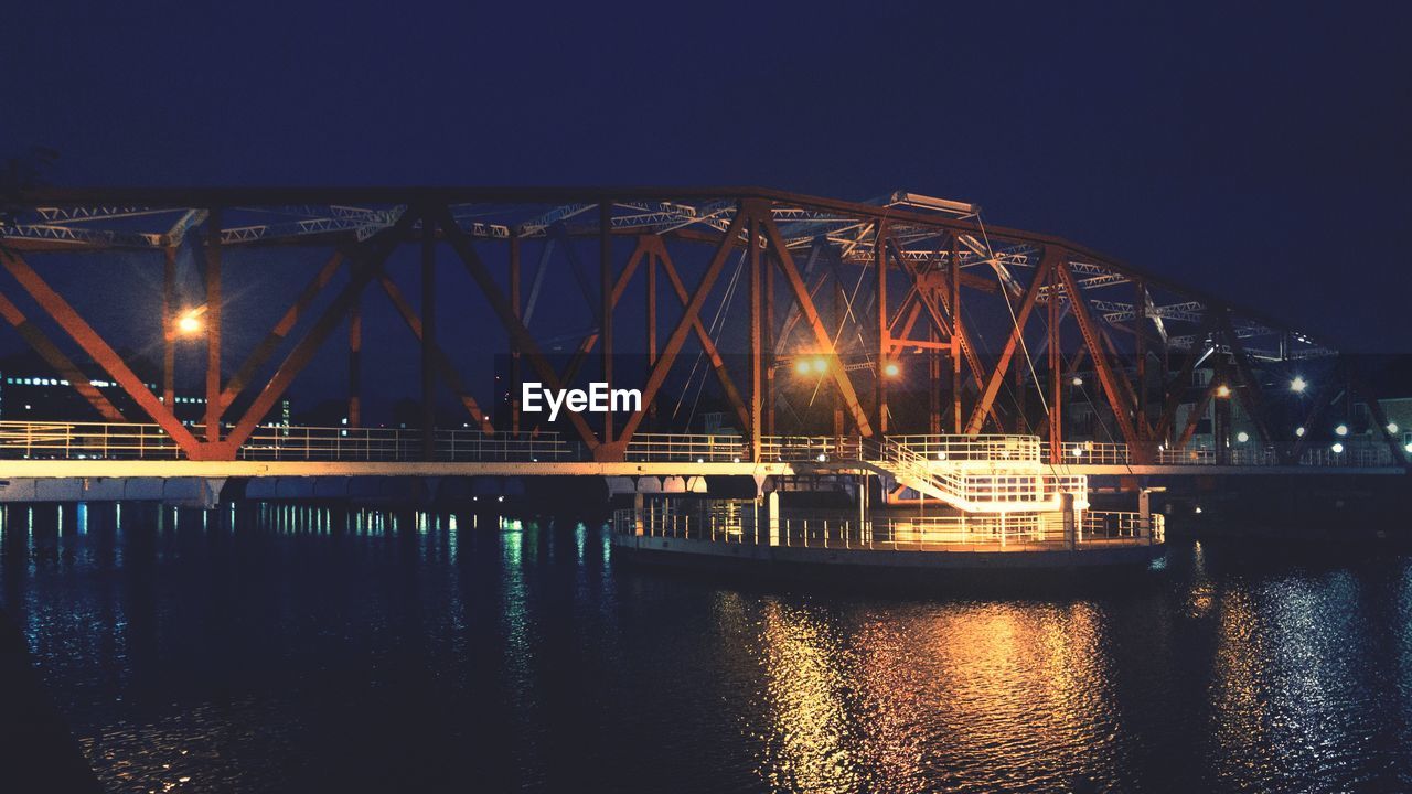 Illuminated bridge over river against sky at night