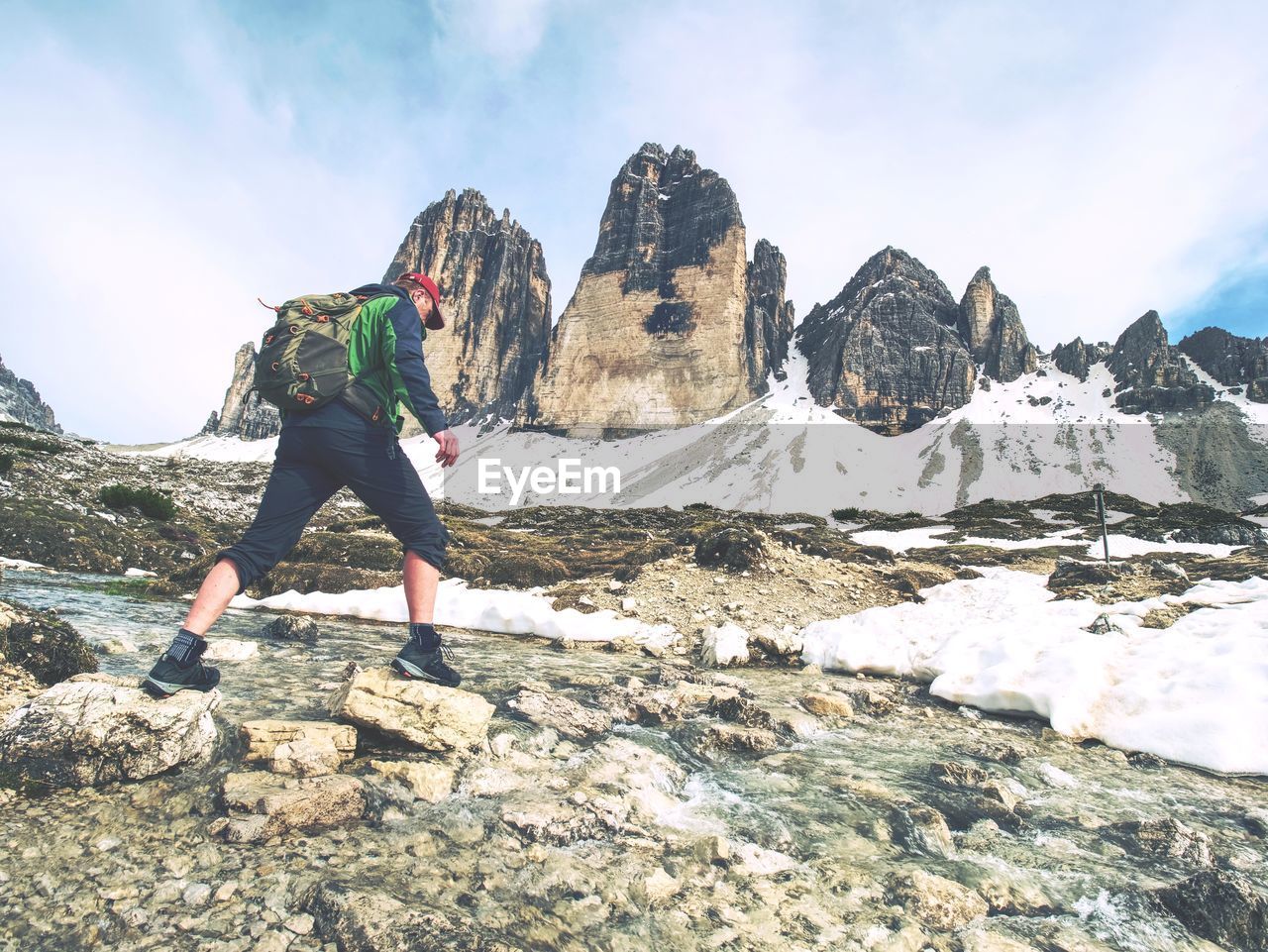 Man trekking in the alps. sharp tre cime peaks stick over the clouds in a beautiful sunny day.