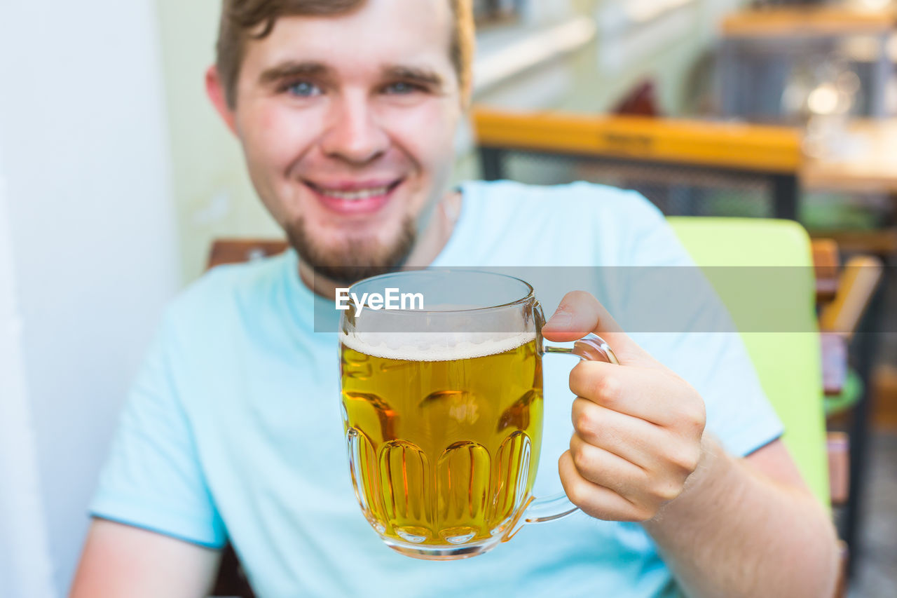 PORTRAIT OF SMILING YOUNG MAN WITH DRINK