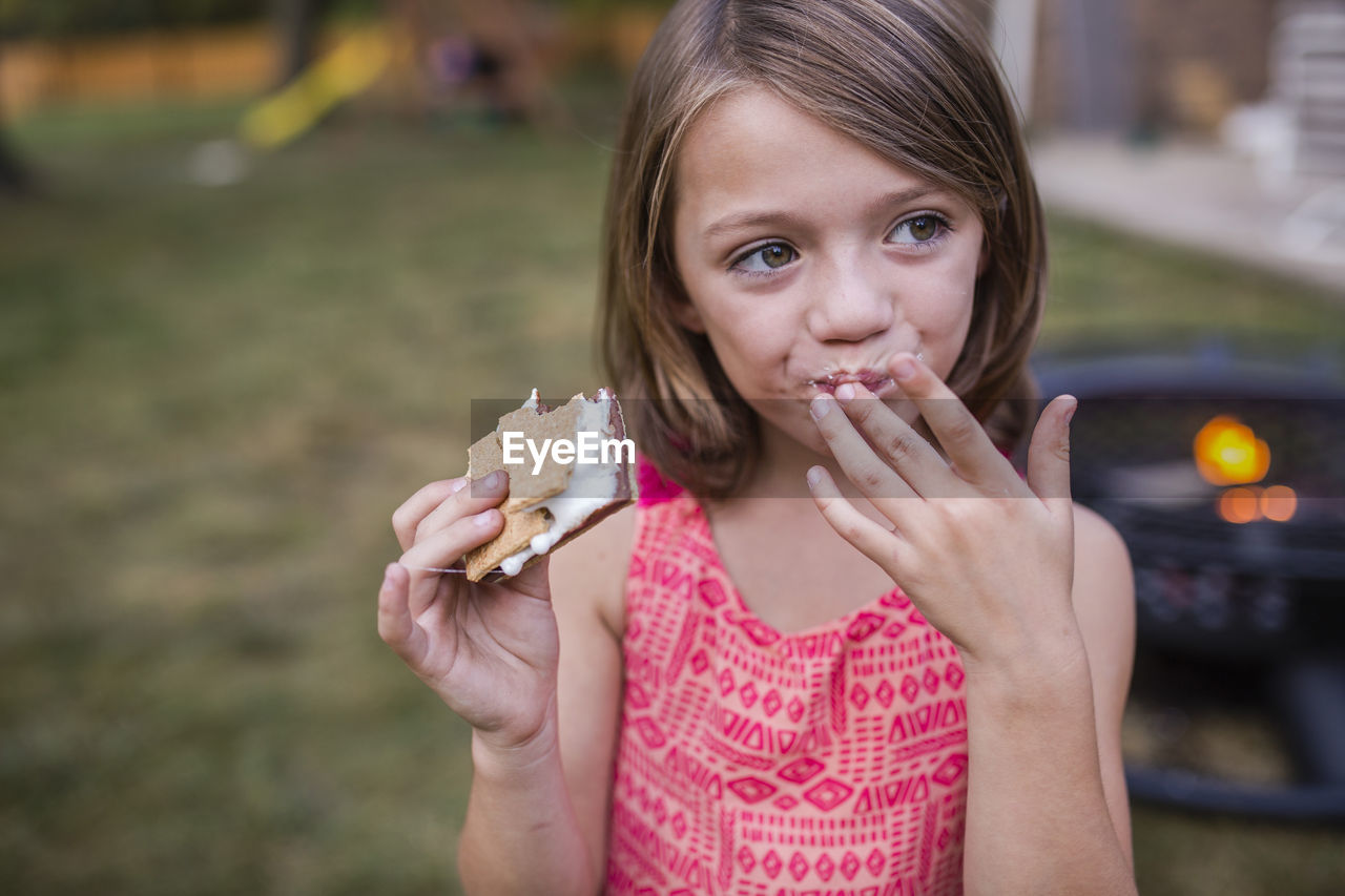 Girl looking away while eating smore at yard