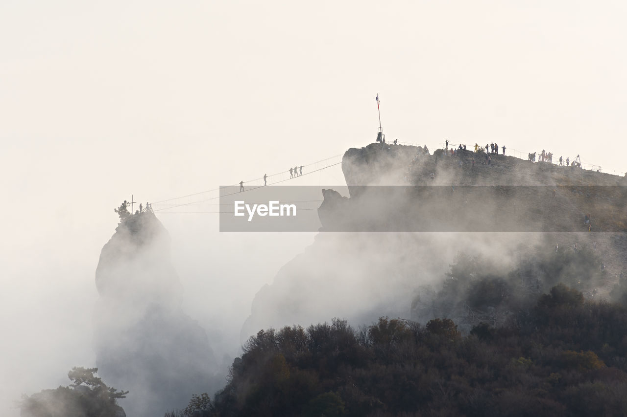 Suspension bridge people. silhouettes of people walking across the bridge through the clouds.