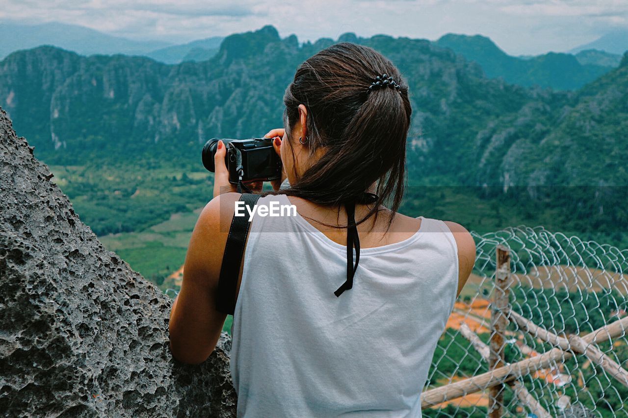 Rear view of woman photographing nature against mountains