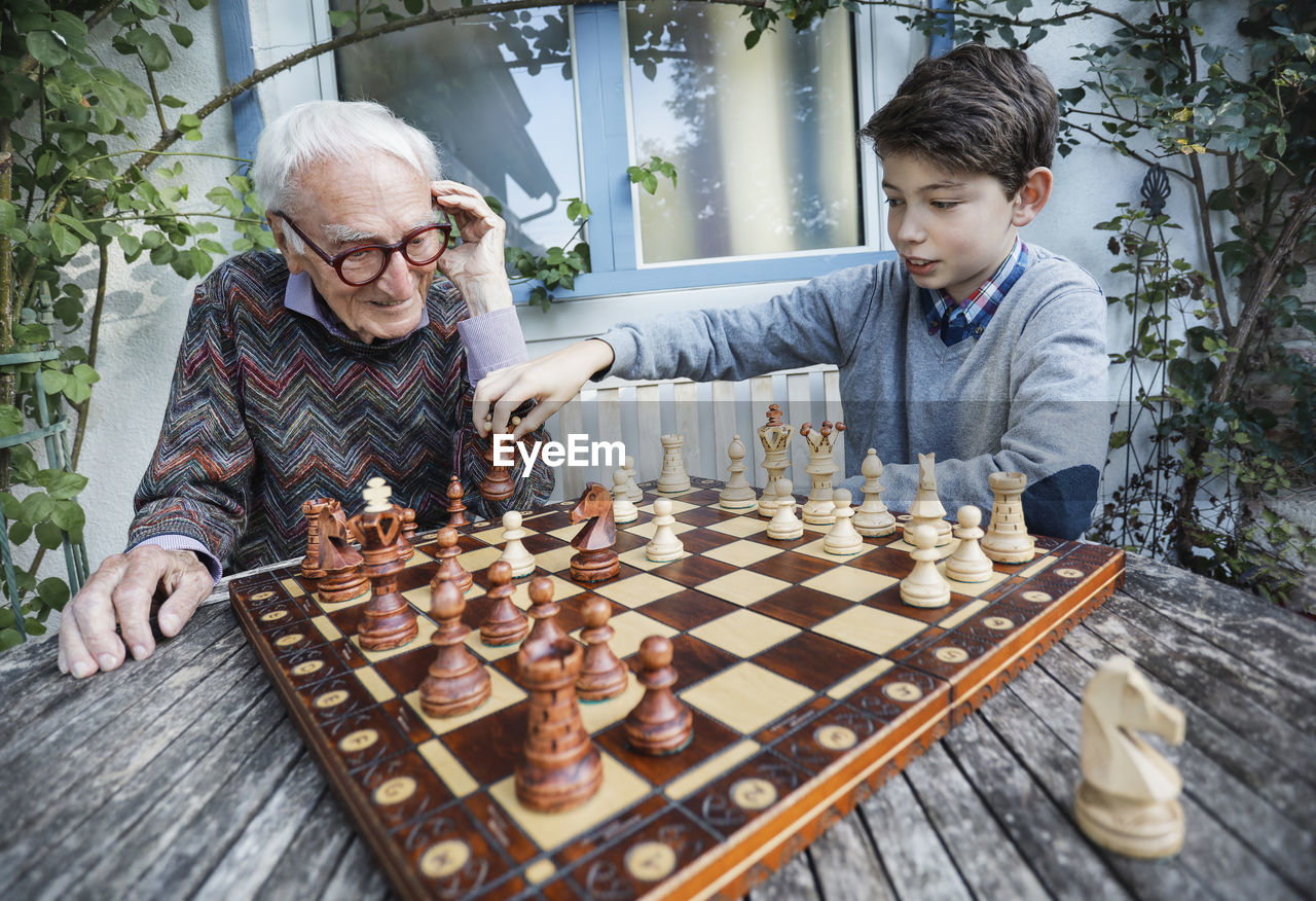Boy playing chess with grandfather in backyard
