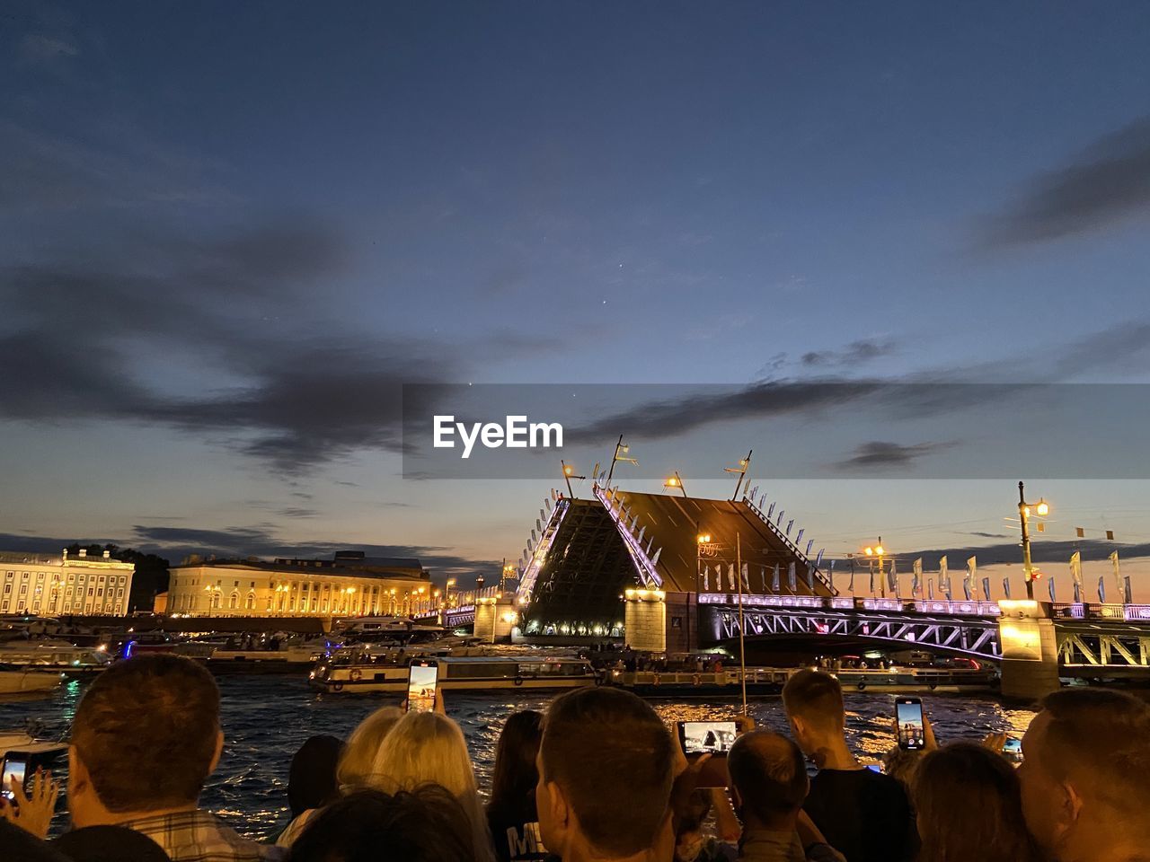 GROUP OF PEOPLE IN ILLUMINATED CITY AGAINST SKY AT NIGHT