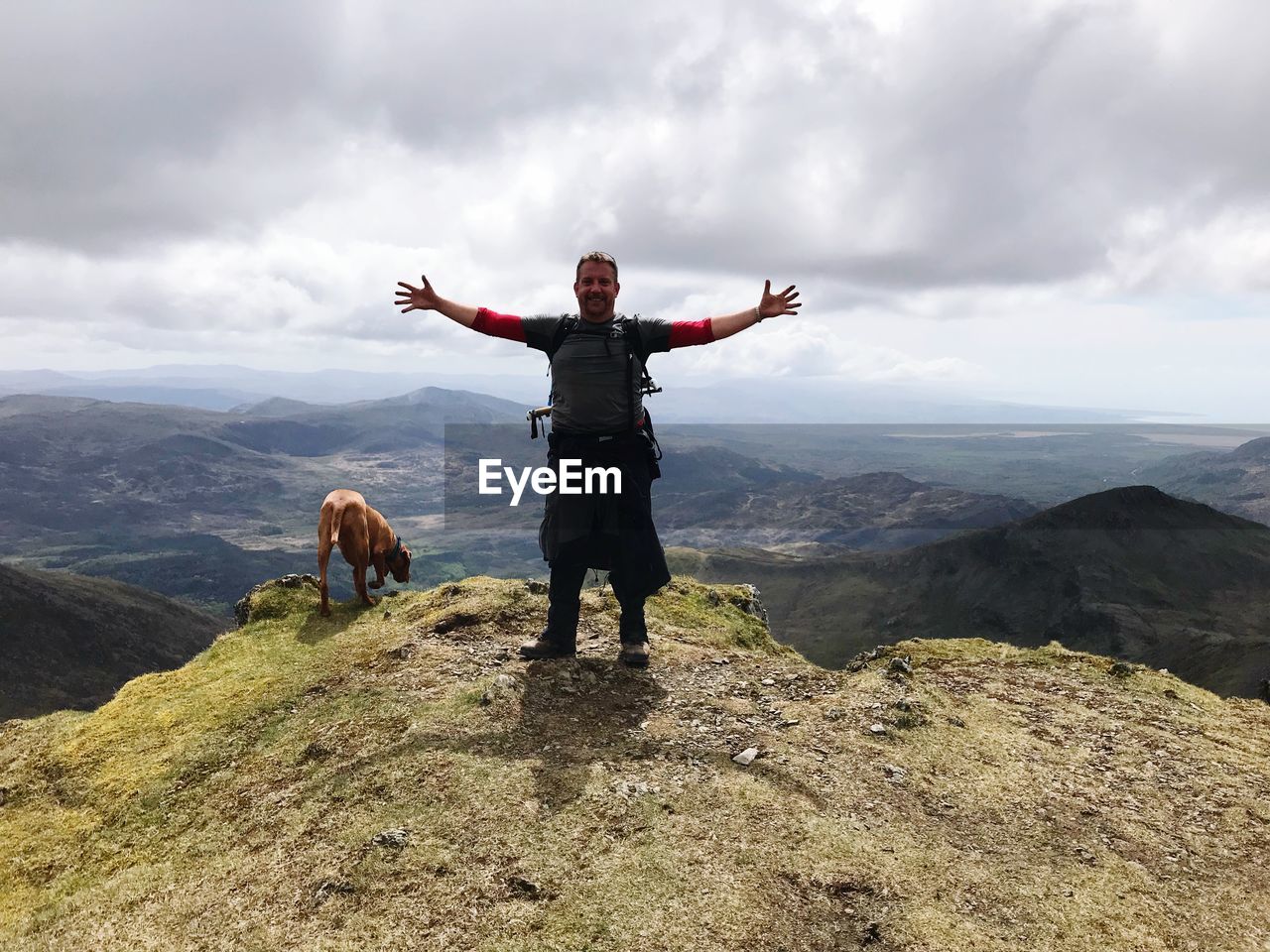 Man with arms outstretched standing on mountain against sky