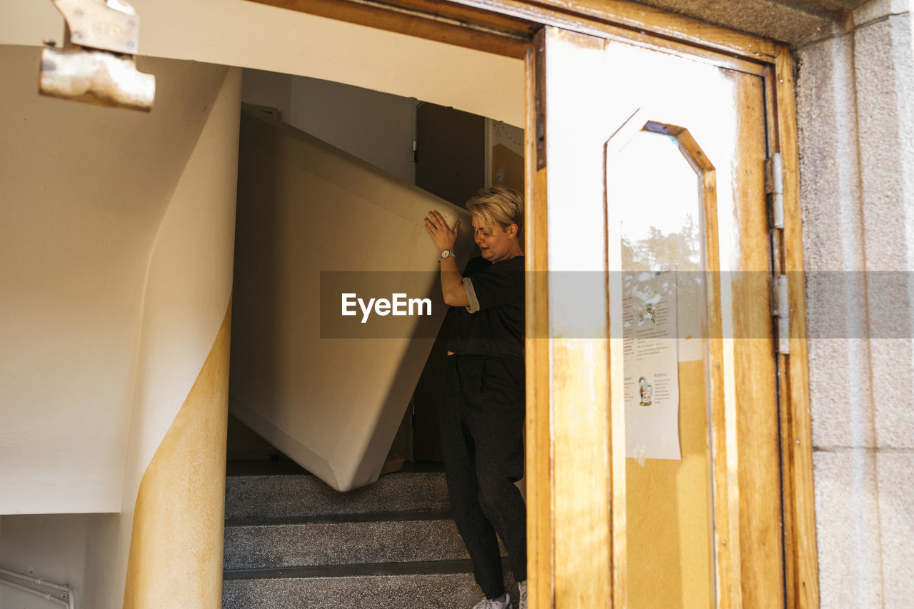 Woman carrying mattress at staircase