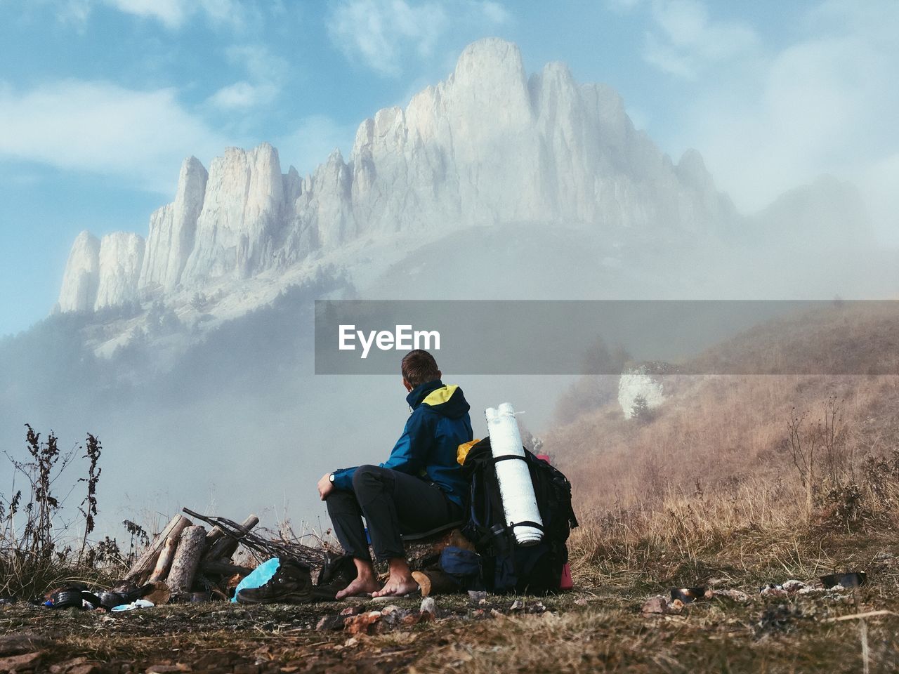 Man sitting on field near mountains during foggy weather