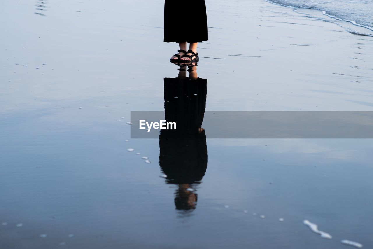 Reflection of woman standing on wet beach