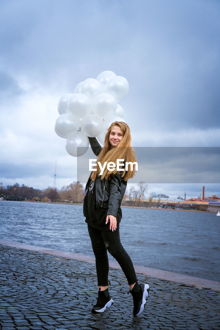 Caucasian girl holding white balloons standing by the river on the embankment