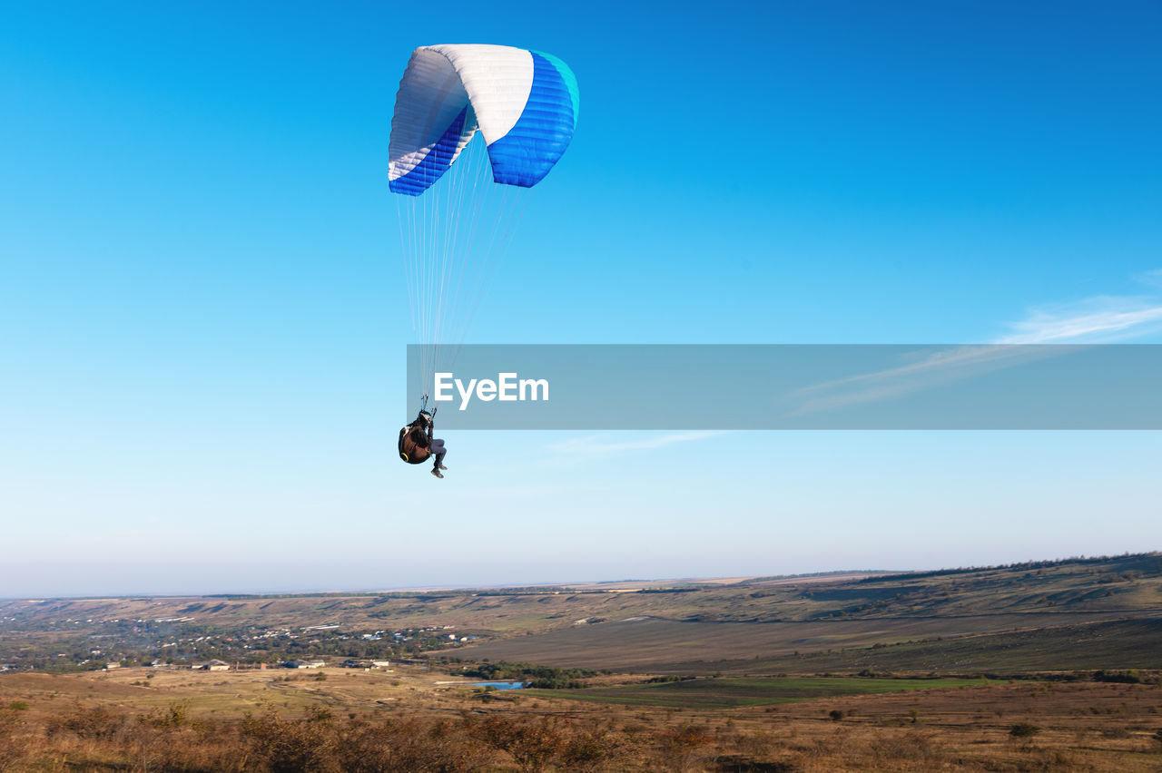 A paraglider takes off from a mountainside with a blue and white canopy and the sun behind. a