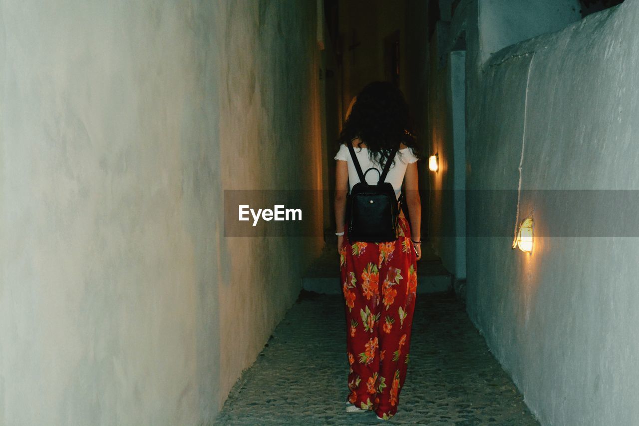 Rear view of woman with backpack standing in alley