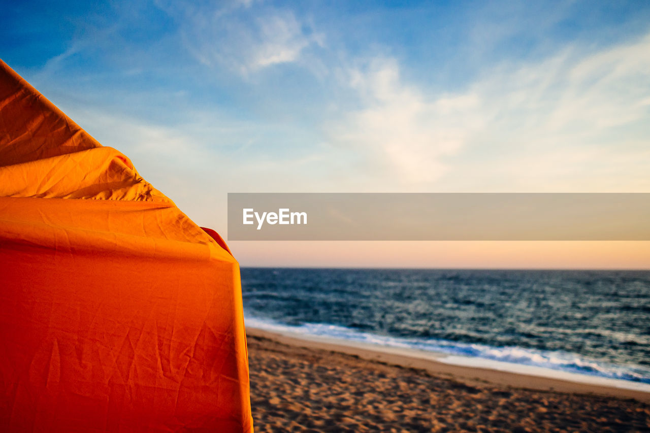 Cropped image of orange parasol at beach against sky during sunset