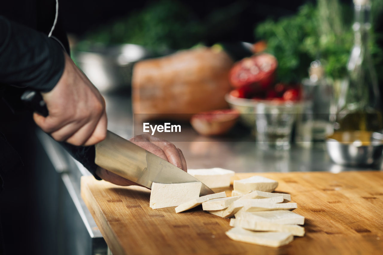 Preparing vegan meal. chef cutting tofu cheese on a wooden cutting board