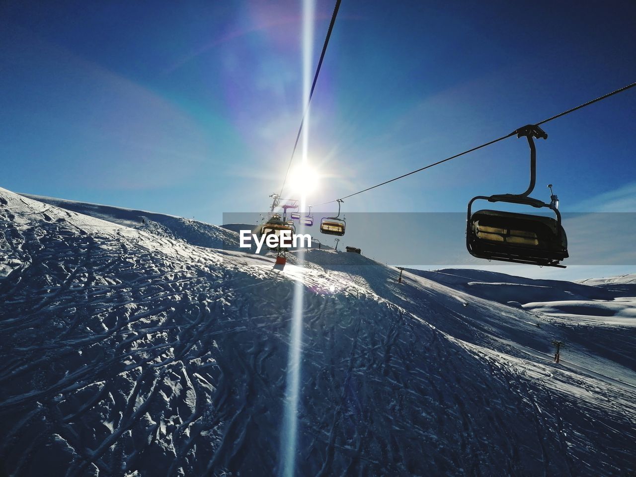 snow, mountain, transportation, winter, cold temperature, nature, sky, sunlight, lens flare, travel, ski lift, mode of transportation, cable car, scenics - nature, skiing, environment, beauty in nature, mountain range, landscape, sun, vacation, sports, day, adventure, piste, winter sports, sunbeam, holiday, overhead cable car, motion, ski, blue, trip, outdoors, ski holiday, clear sky, sunny, non-urban scene, travel destinations, snowcapped mountain, land, journey