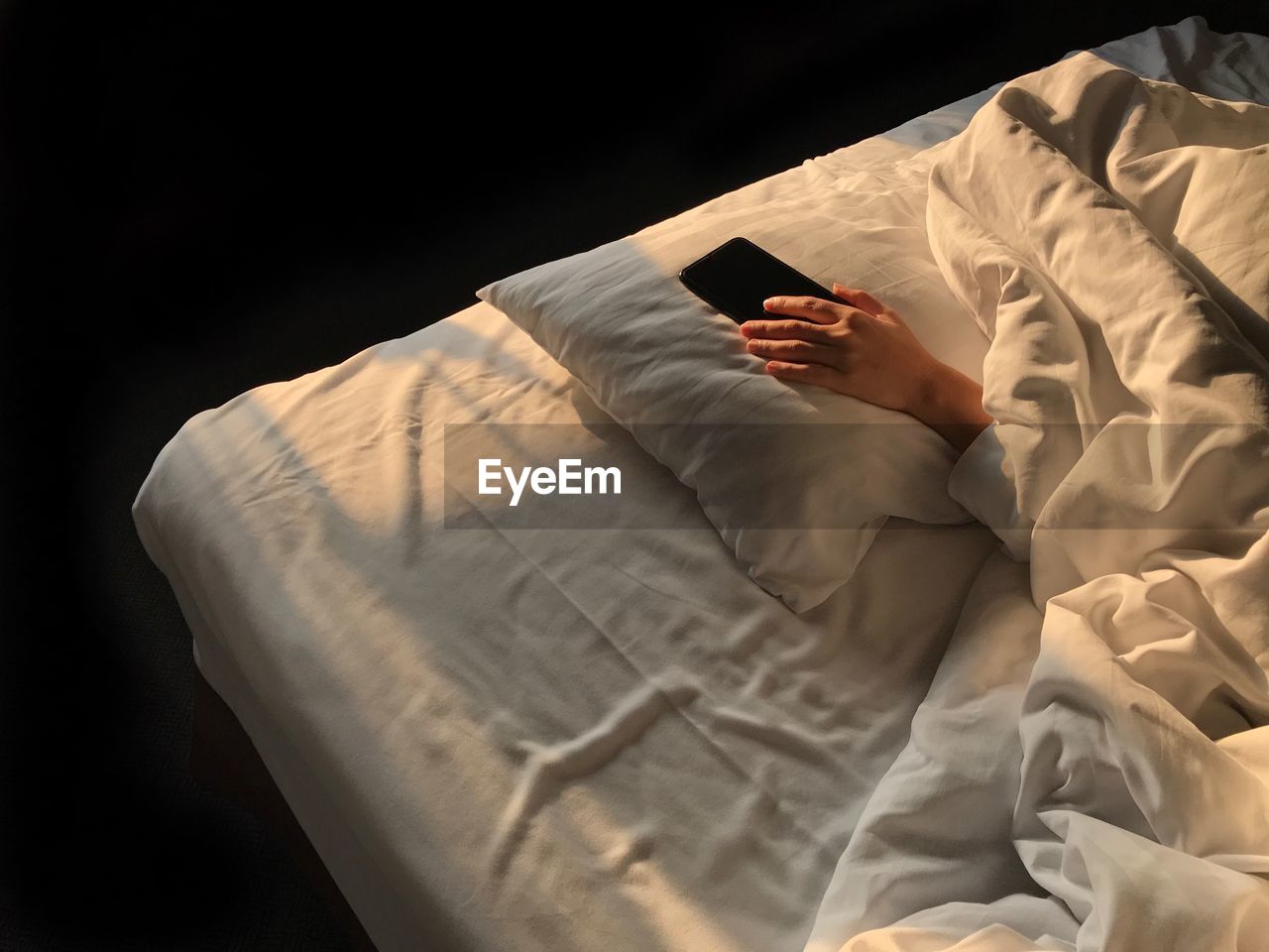 High angle view of cropped hand holding mobile phone on bed