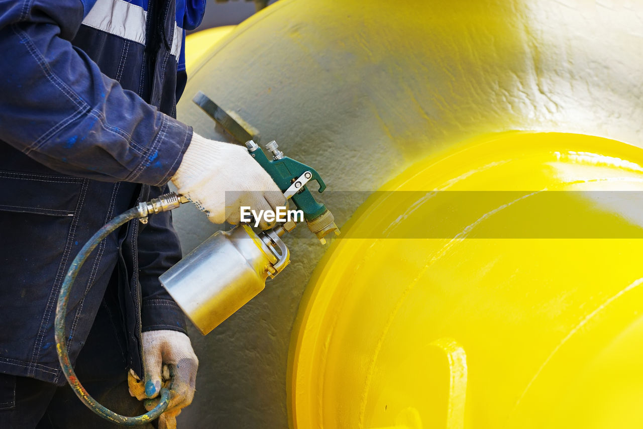 Midsection of man working on yellow pipe