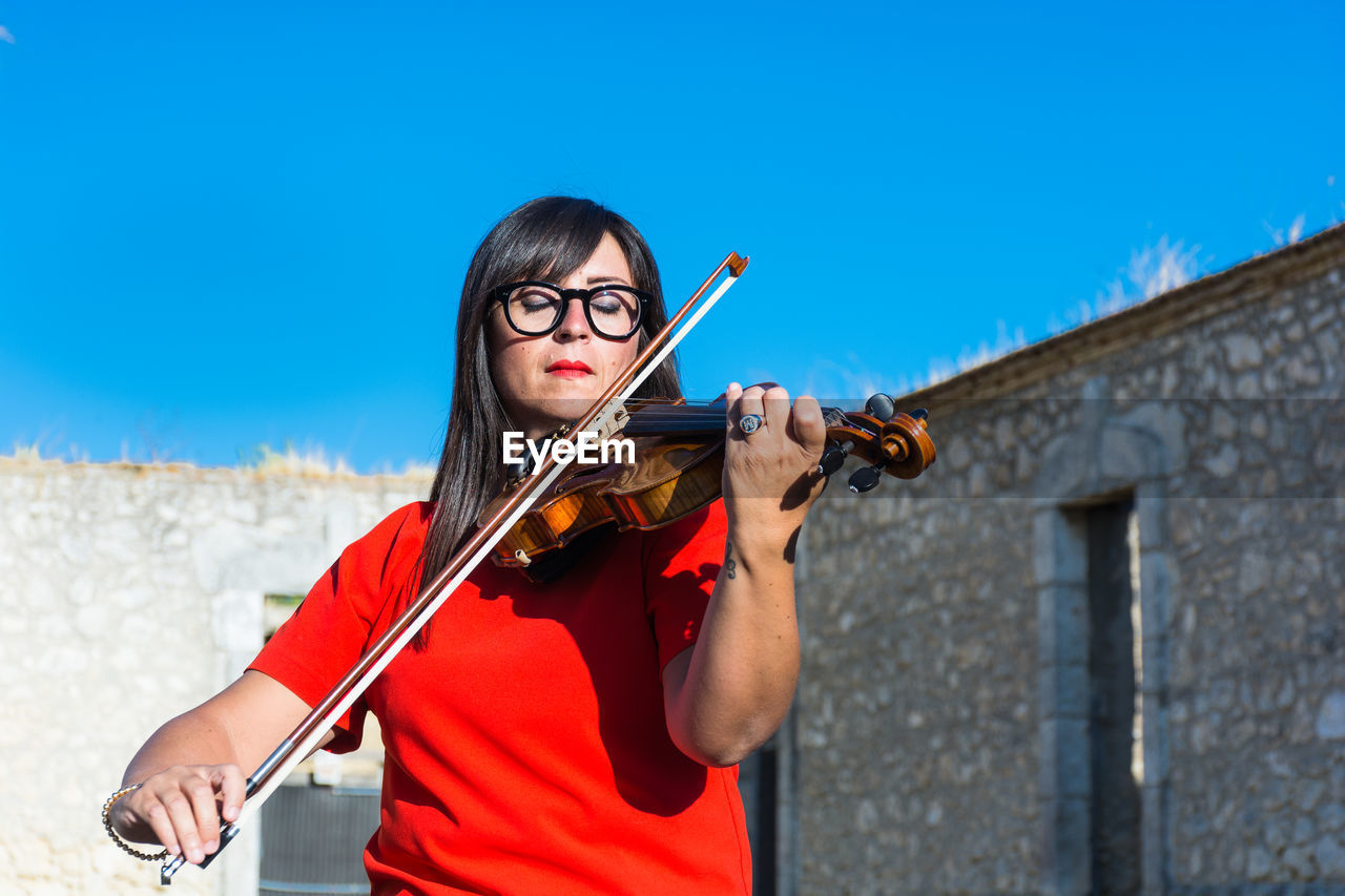 Woman playing violin while standing against built structure