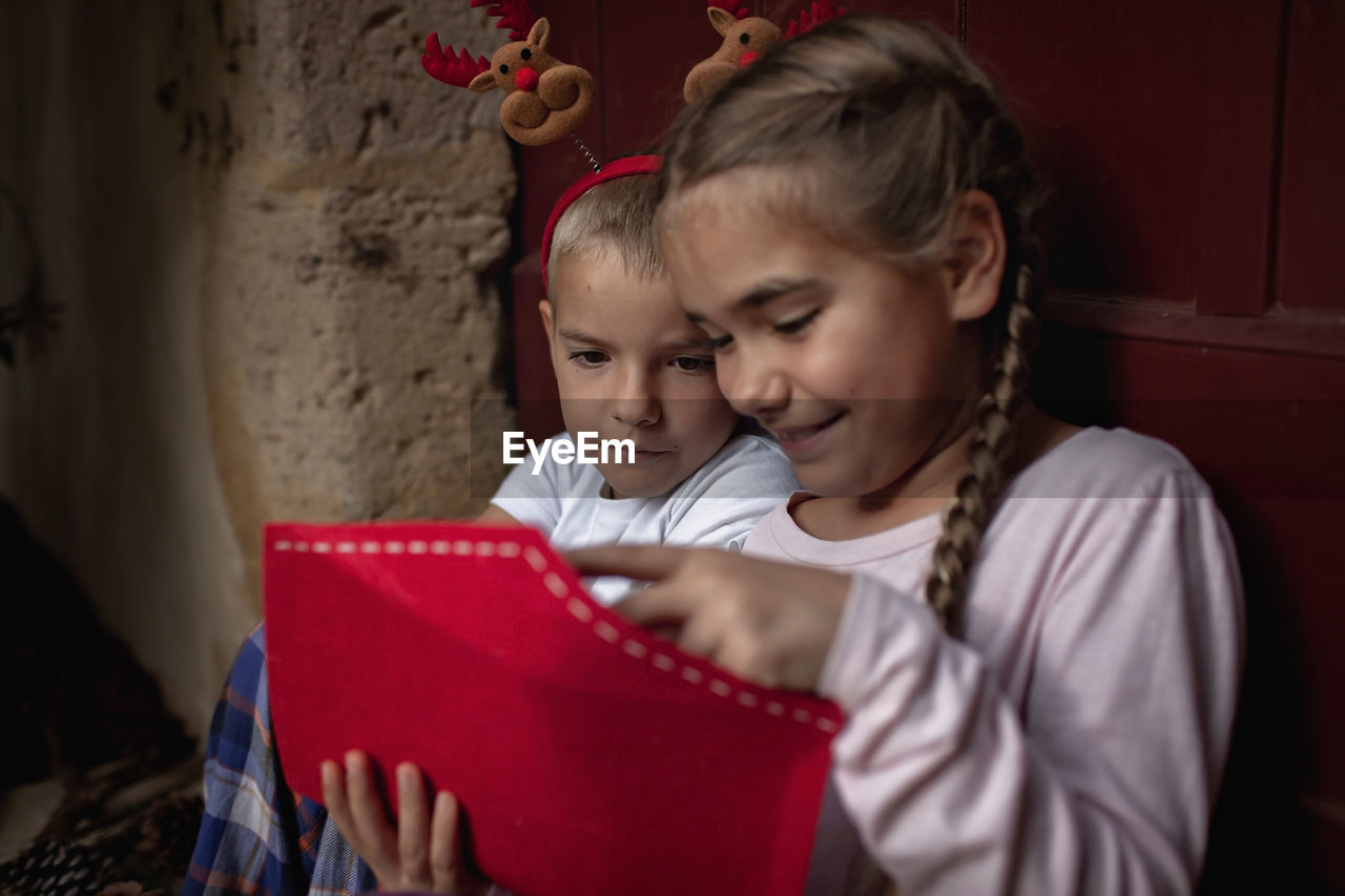 Siblings in fun hat write letter for santa and dreamily wait for gifts on christmas, winter holidays