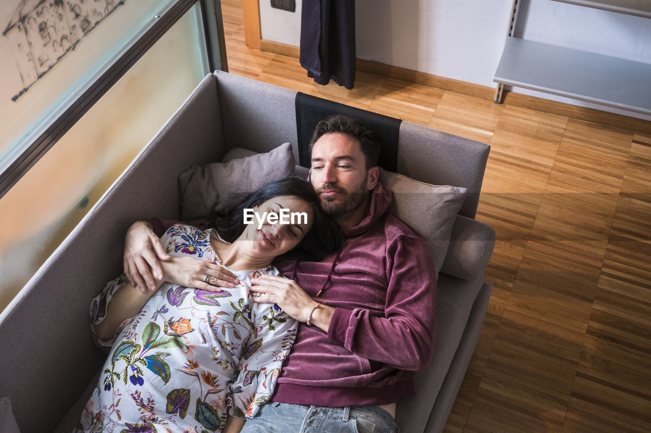 High angle view of couple lying down on sofa at home