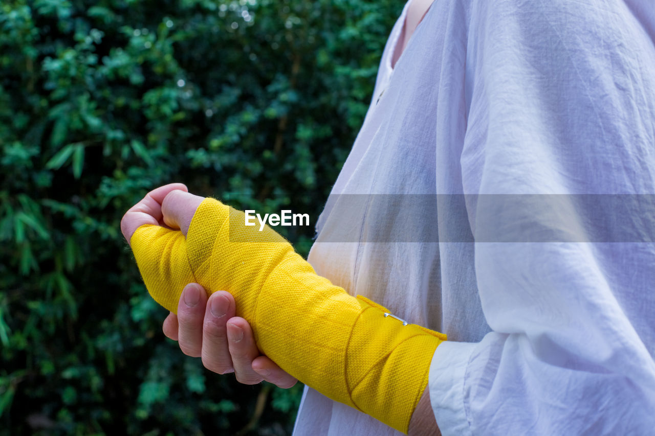 Midsection of woman wearing bandage while standing against plants