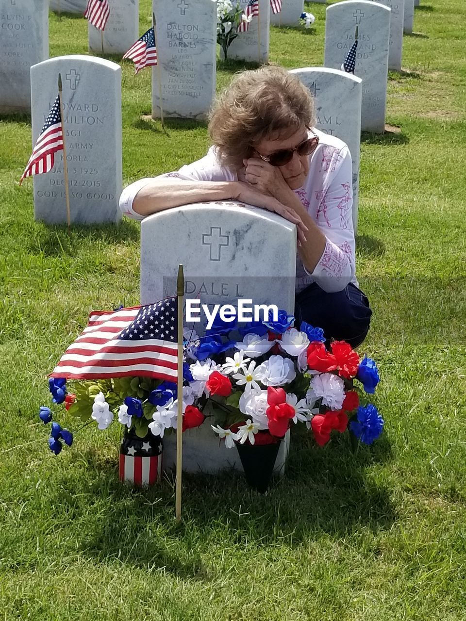 REAR VIEW OF MAN SITTING ON GRASSY FIELD BY FLAG