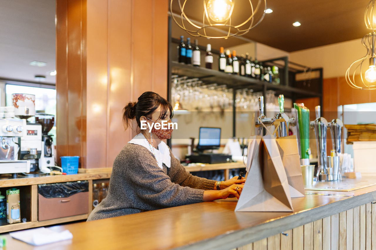 Female owner keeping take out food ready in brown bag on restaurant counter