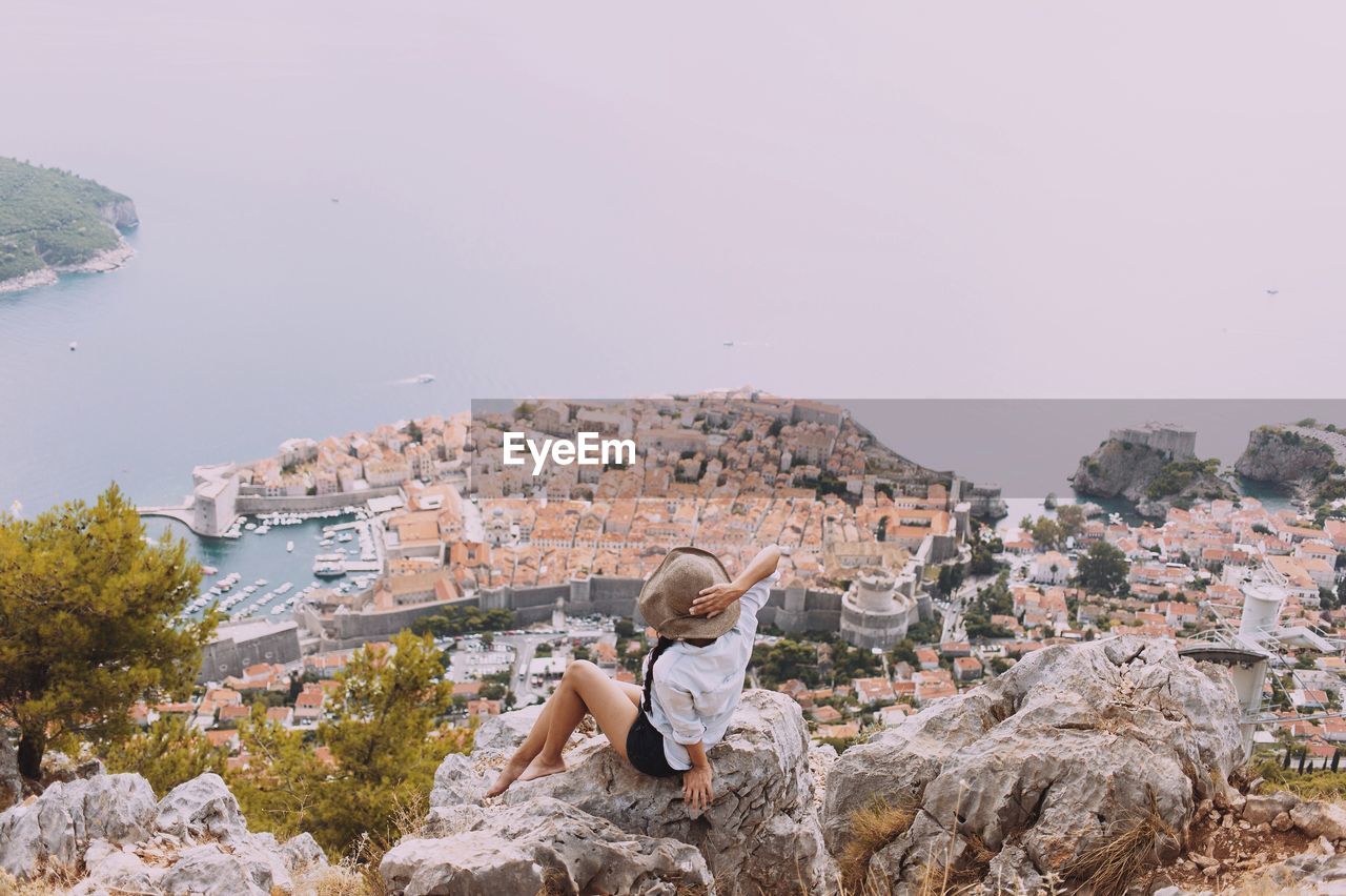 High angle view of woman sitting on rock against old town by sea