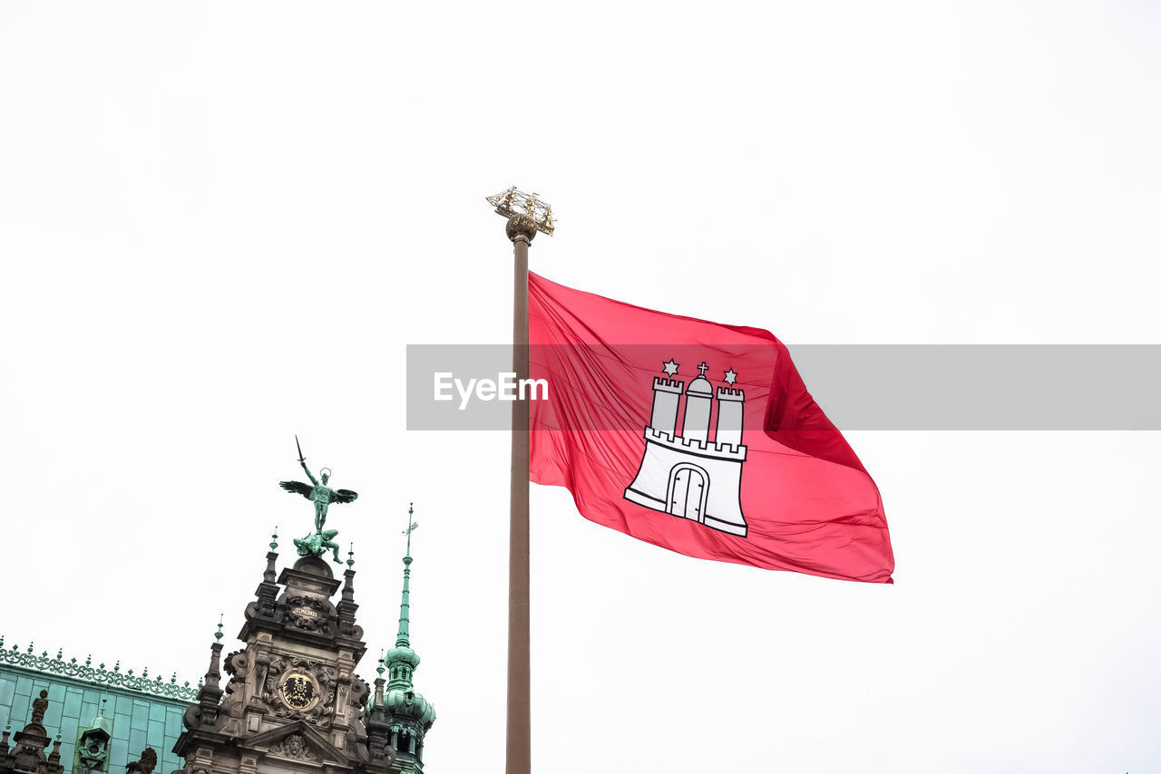 LOW ANGLE VIEW OF RED FLAG ON STATUE AGAINST SKY