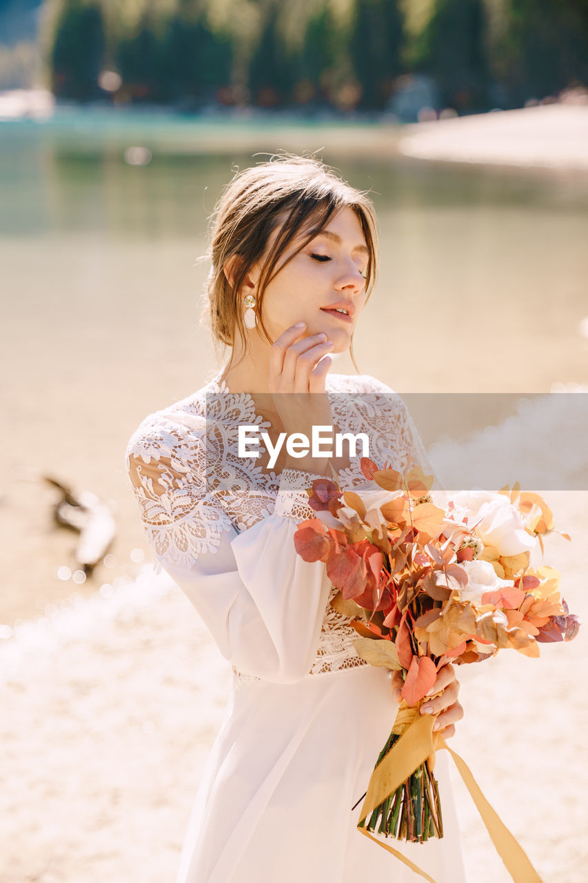 Bride holding bouquet looking away by riverbank