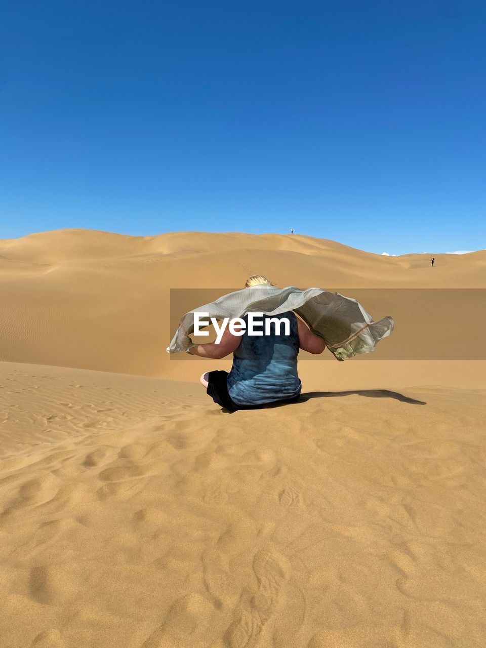 Woman with scarfs on sand dune in desert against clear blue sky