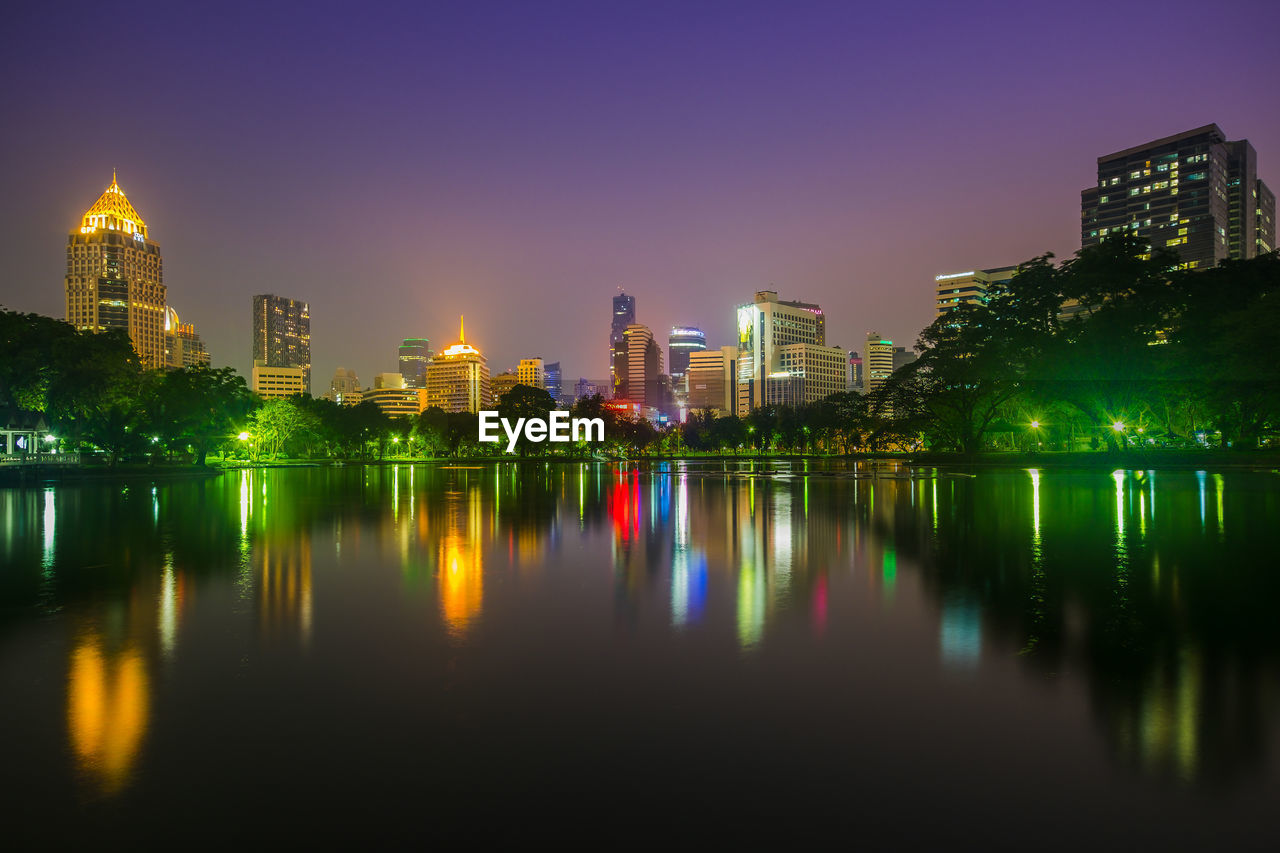 Illuminated buildings by river against sky at night