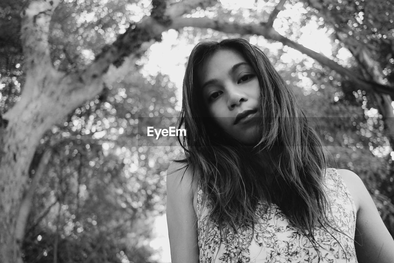 PORTRAIT OF YOUNG WOMAN AGAINST TREE