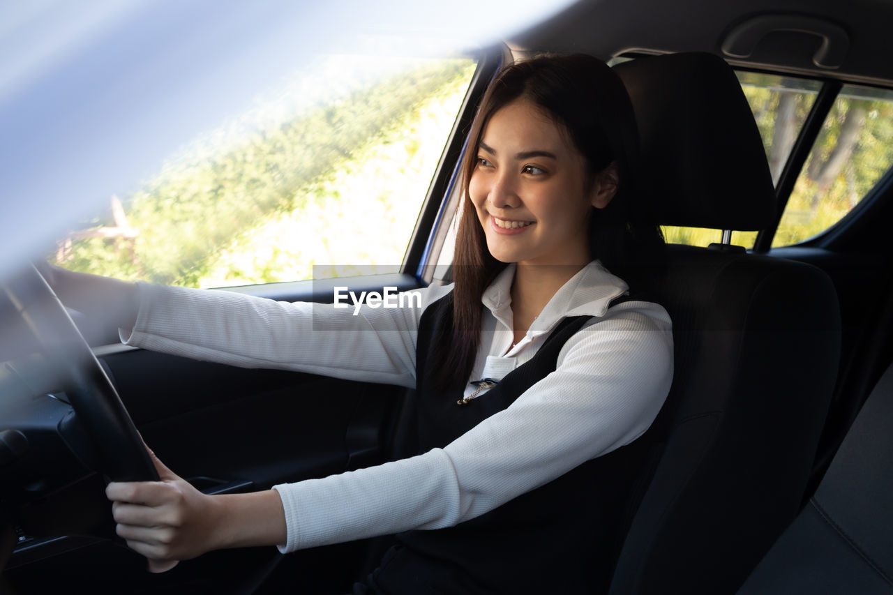 PORTRAIT OF A SMILING YOUNG WOMAN SITTING IN CAR