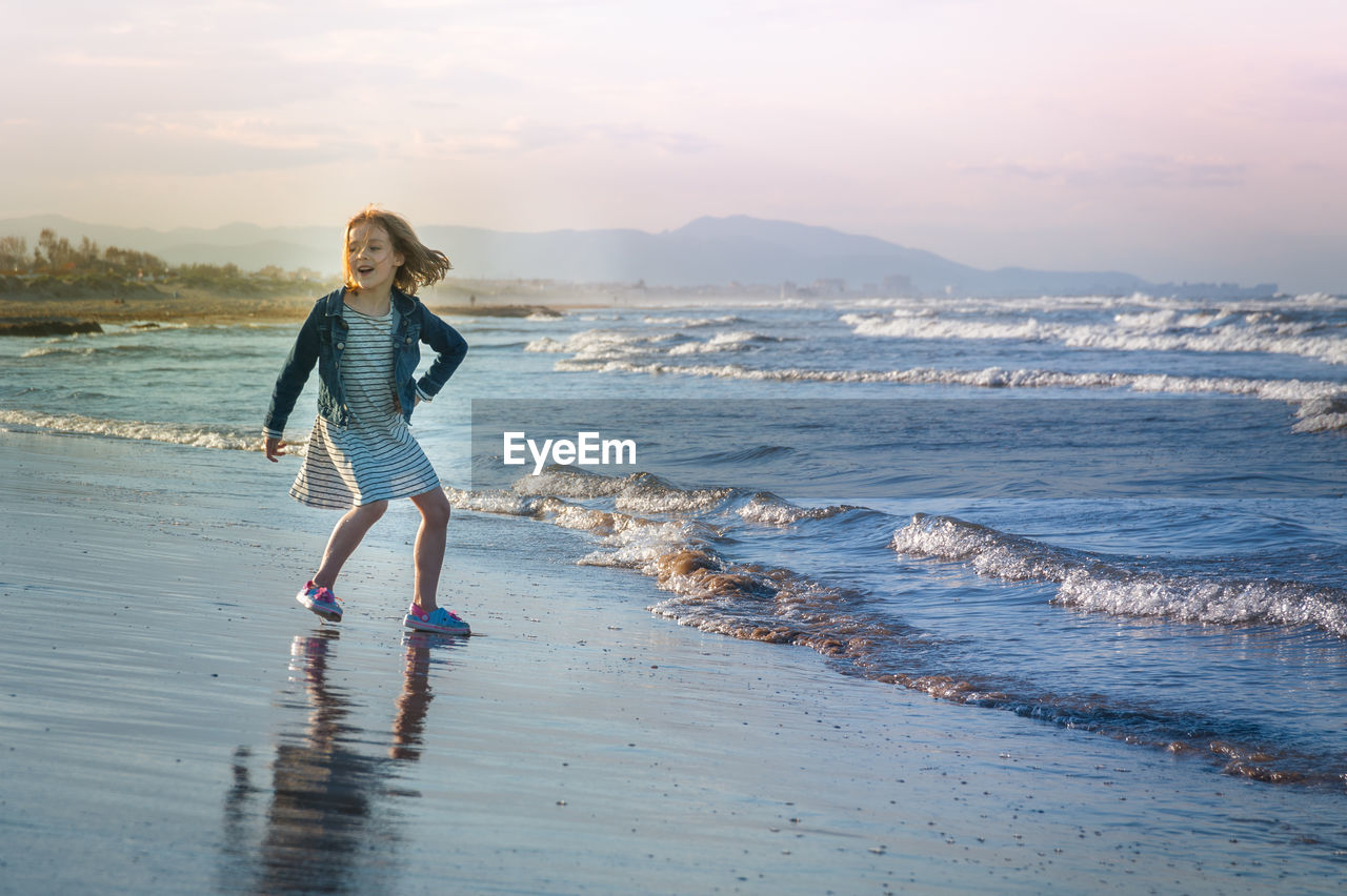 Girl running while playing on beach against sky during sunset