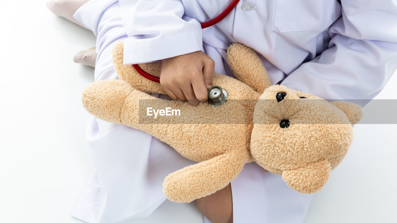 Little asian girl playing doctor and listening teddy bear with stethoscope, asian girl