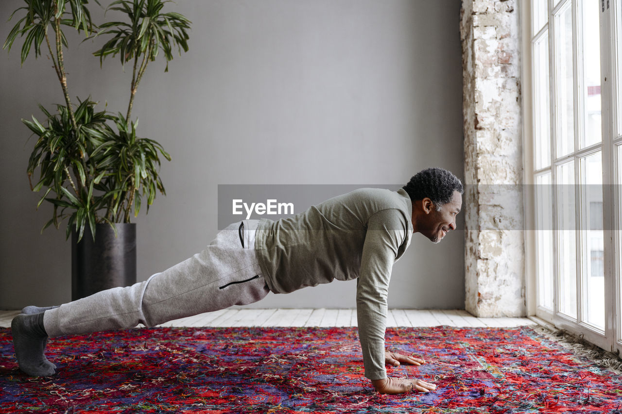 Smiling man practicing planks on carpet at home