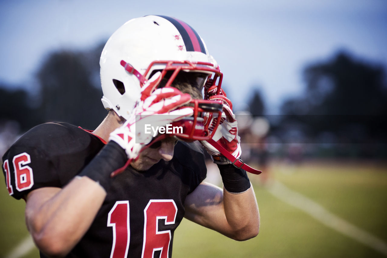 Close-up of teenage american football player holding helmet at field