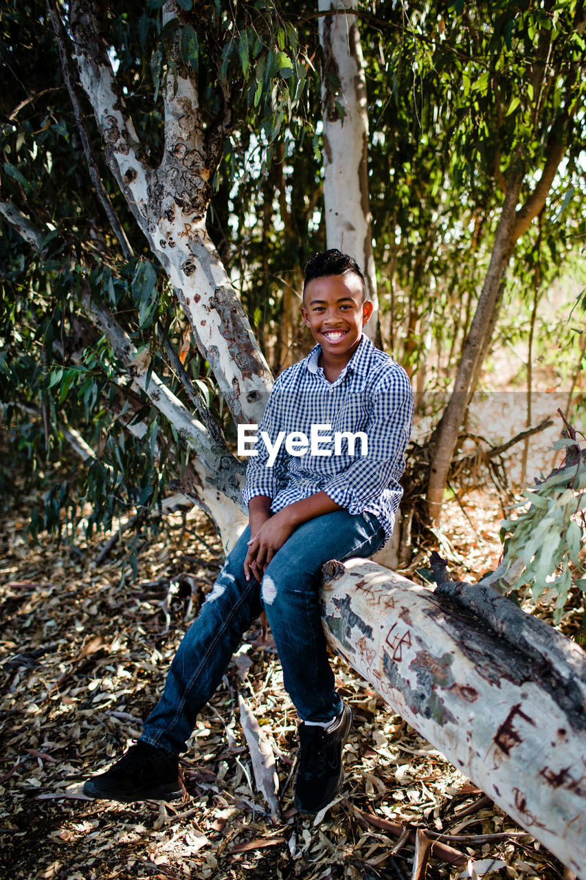 Young boy posing in tree & smiling for camera at park in chula vista