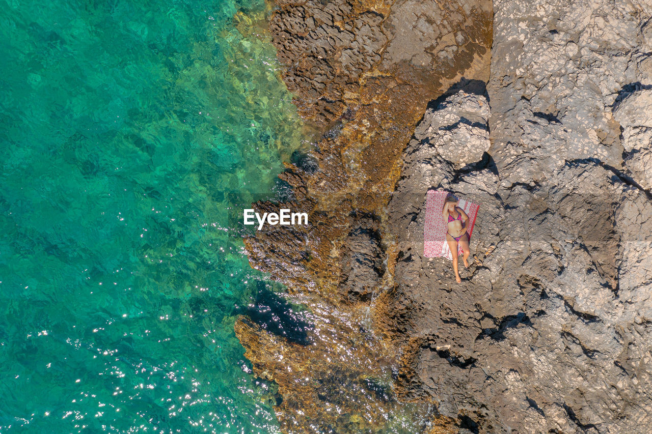 Aerial view of a girl sunbathing on the rocky beach, paklinski otoci islands in hvar, adriatic sea