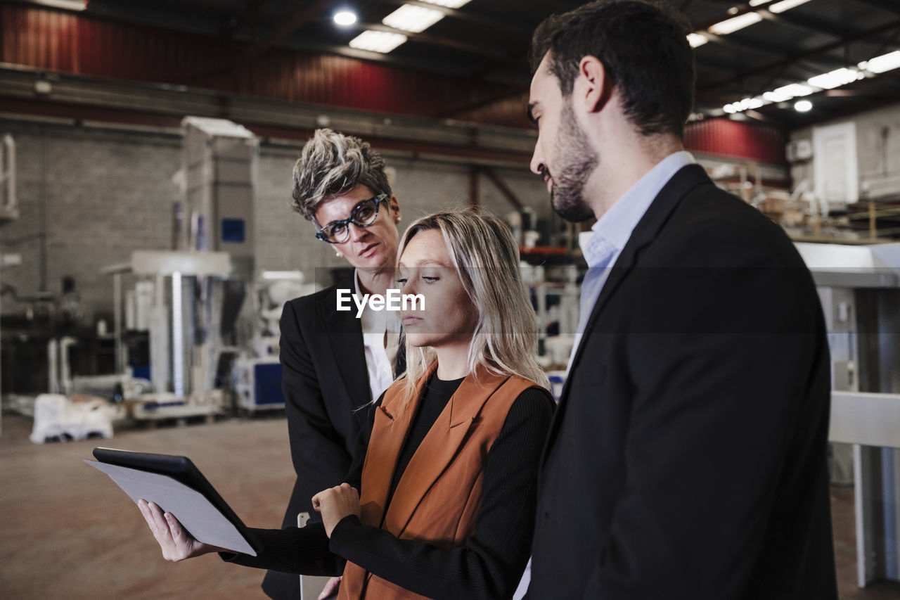 Young businesswoman discussing over tablet pc with colleagues at industry