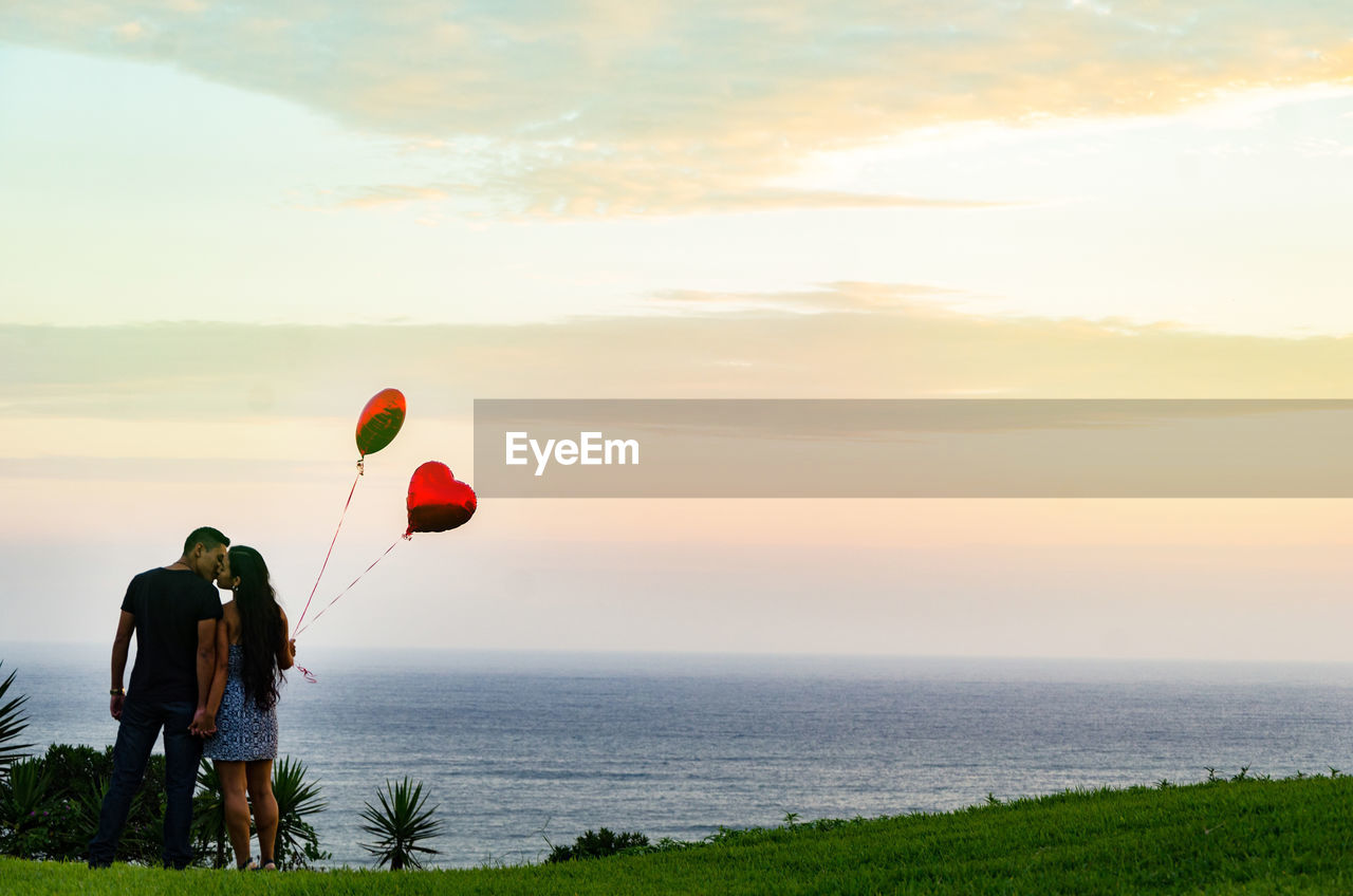 REAR VIEW OF PEOPLE ON THE SEA AT SUNSET