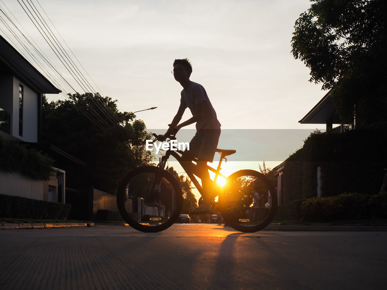 Low angle view of boy riding bicycle on street against sky during sunset