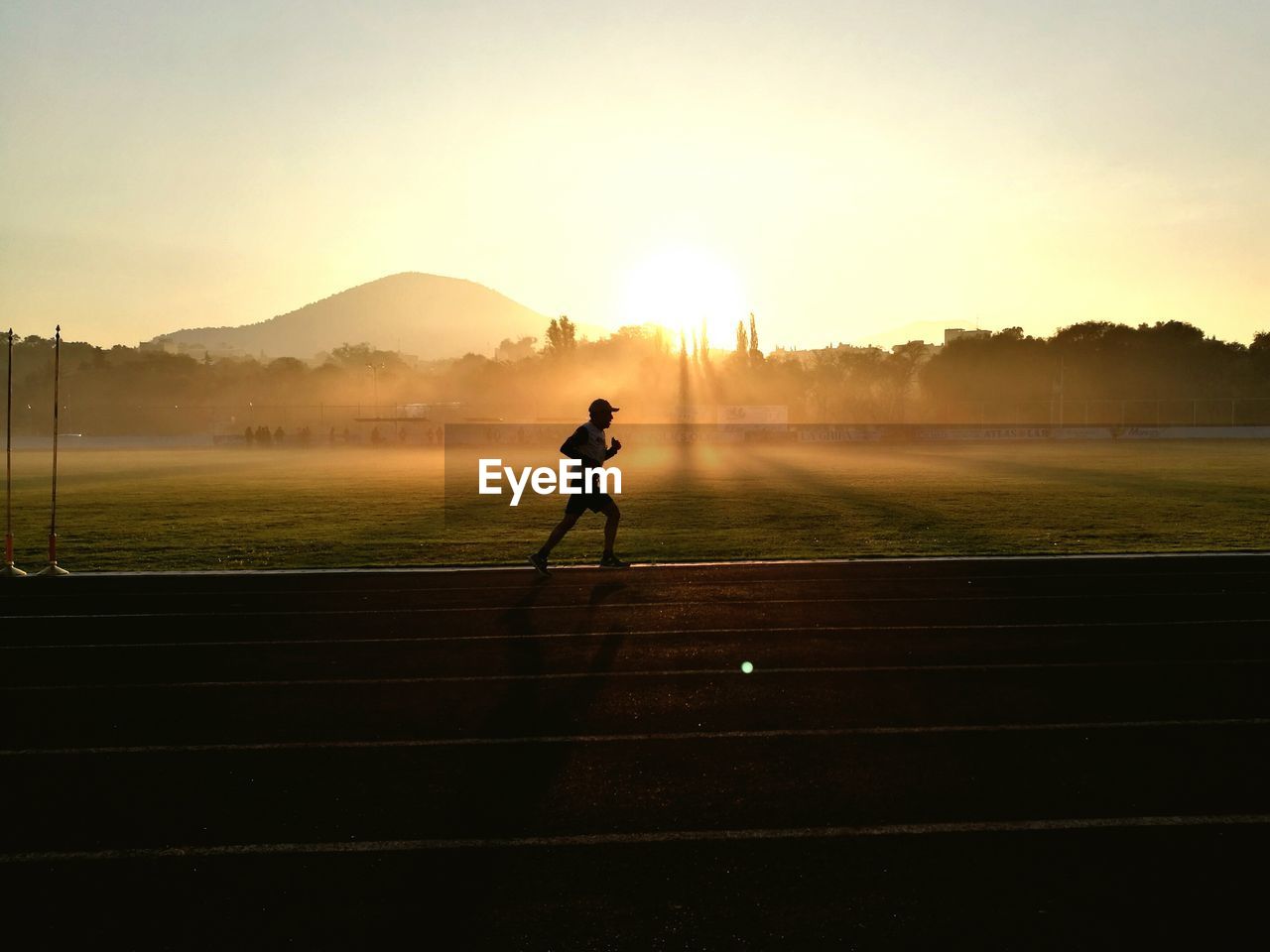 Man running on sports track against sky during sunset