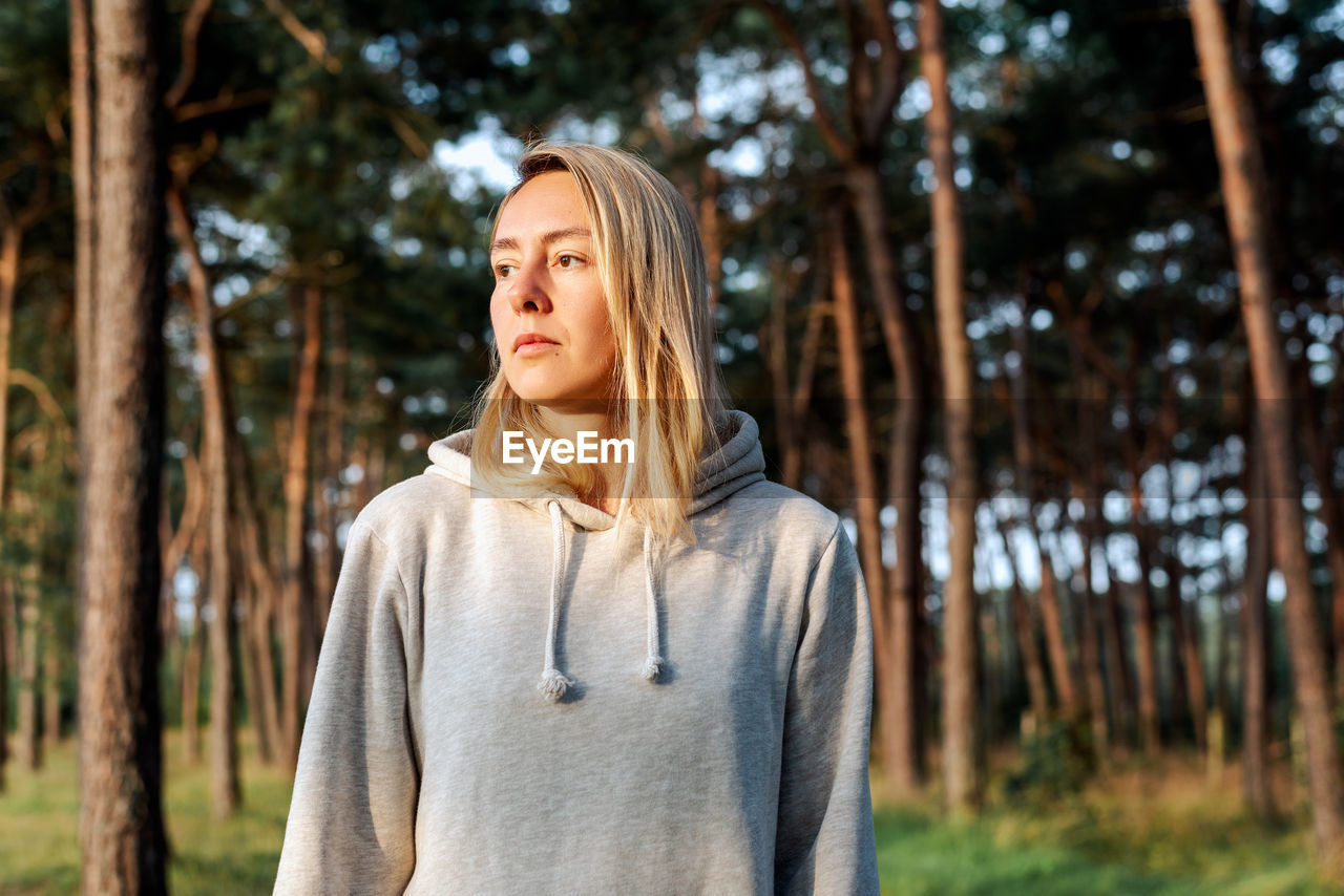 Portrait of a young blond woman walking in a pine forest at dawn.