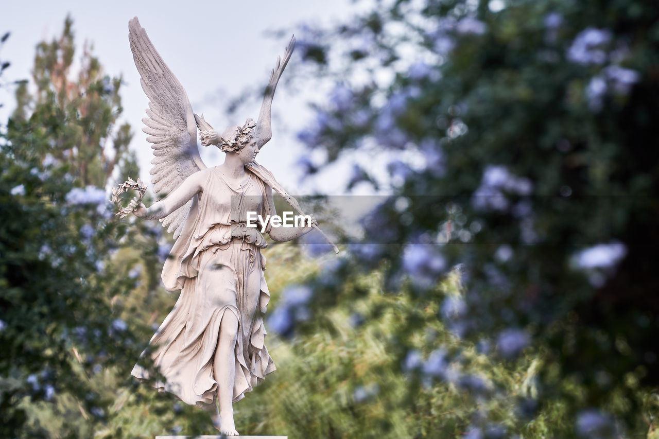 Low angle view of angel statue against trees